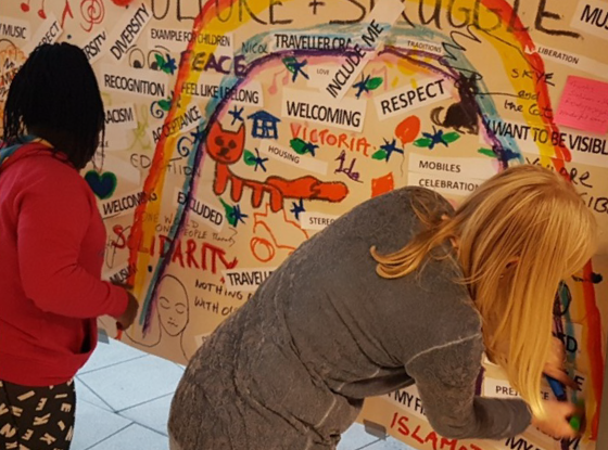 rear view of two women working on a multicolour mural with text and a rainbow