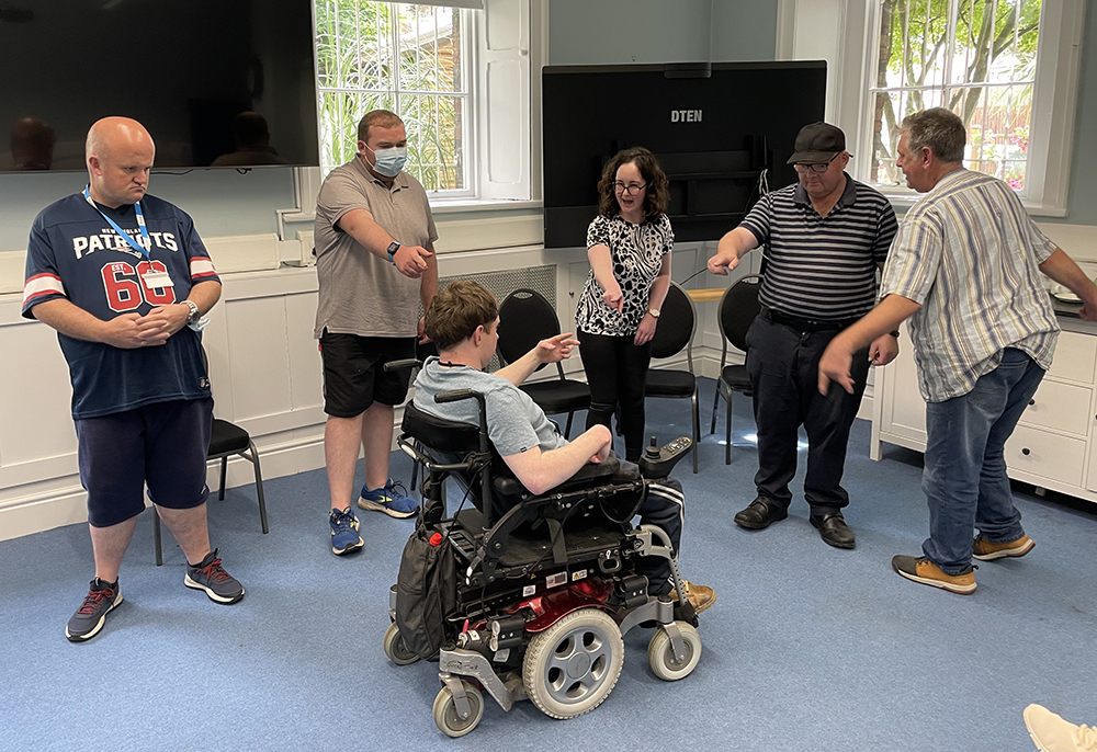 group of people standing in a room, with a person in a wheelchair